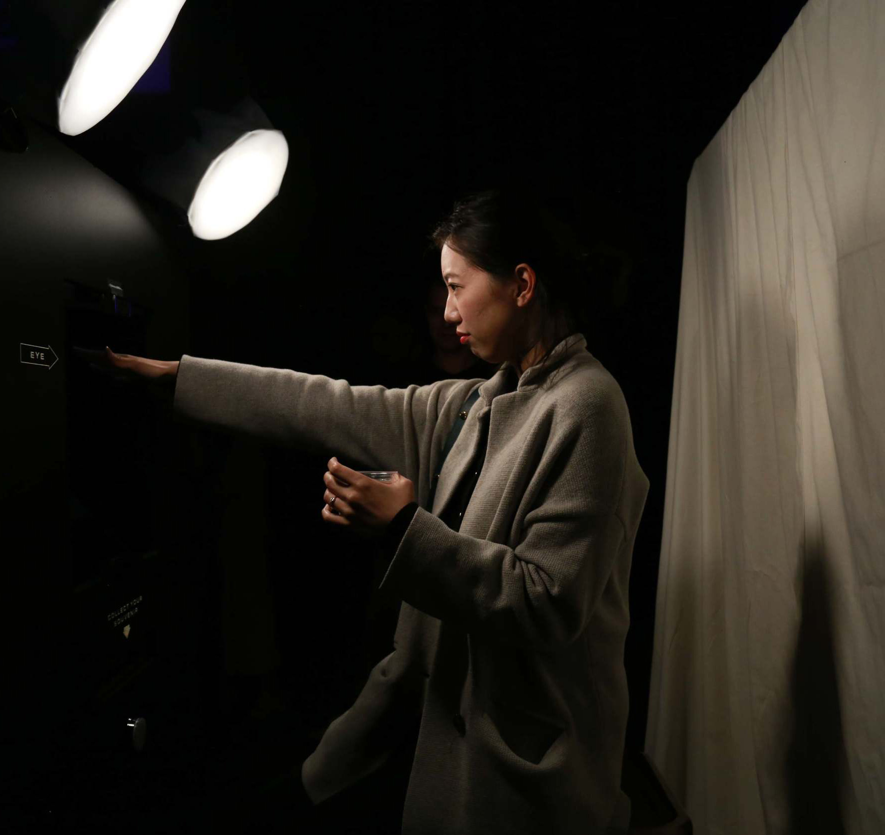 A woman, dramatically lit by spotlights, interacts with the photo booth installation with an outstretched arm.
